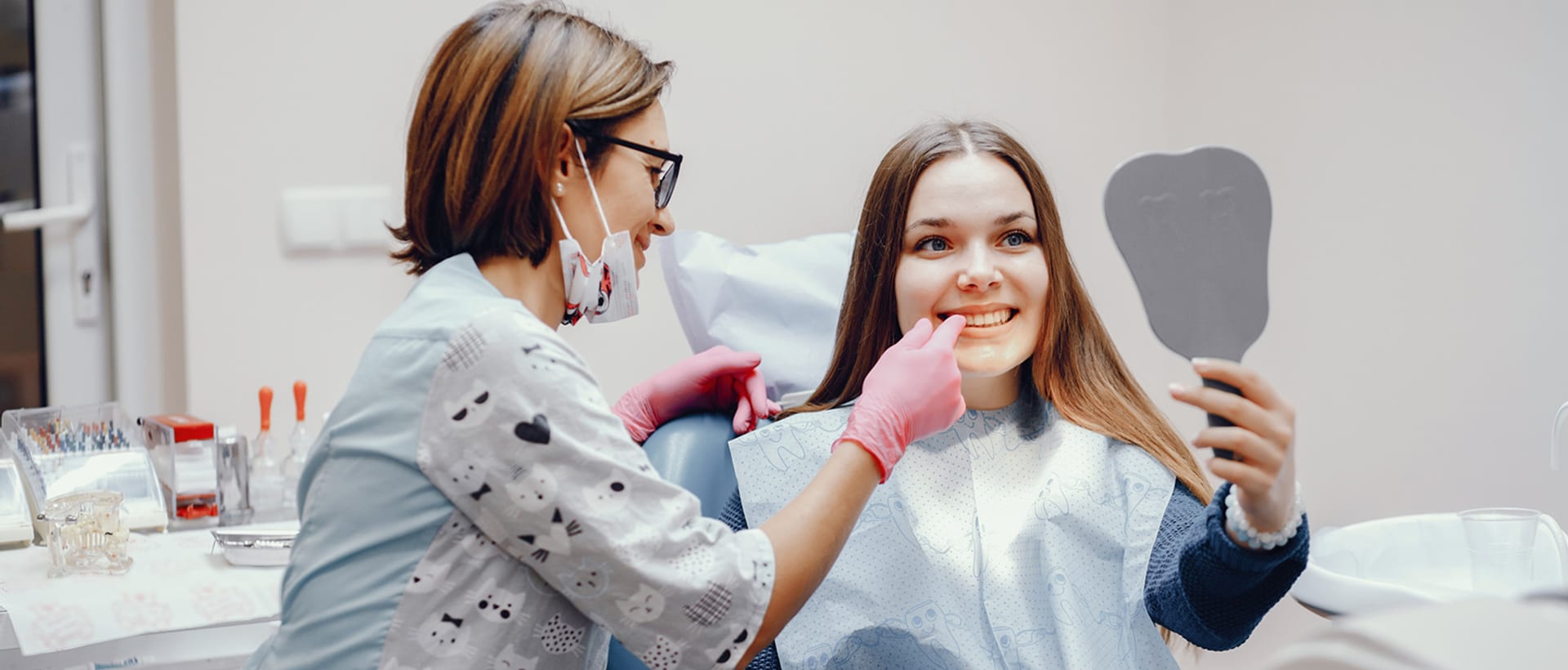 Patient smiling into a hand mirror beside her dentist